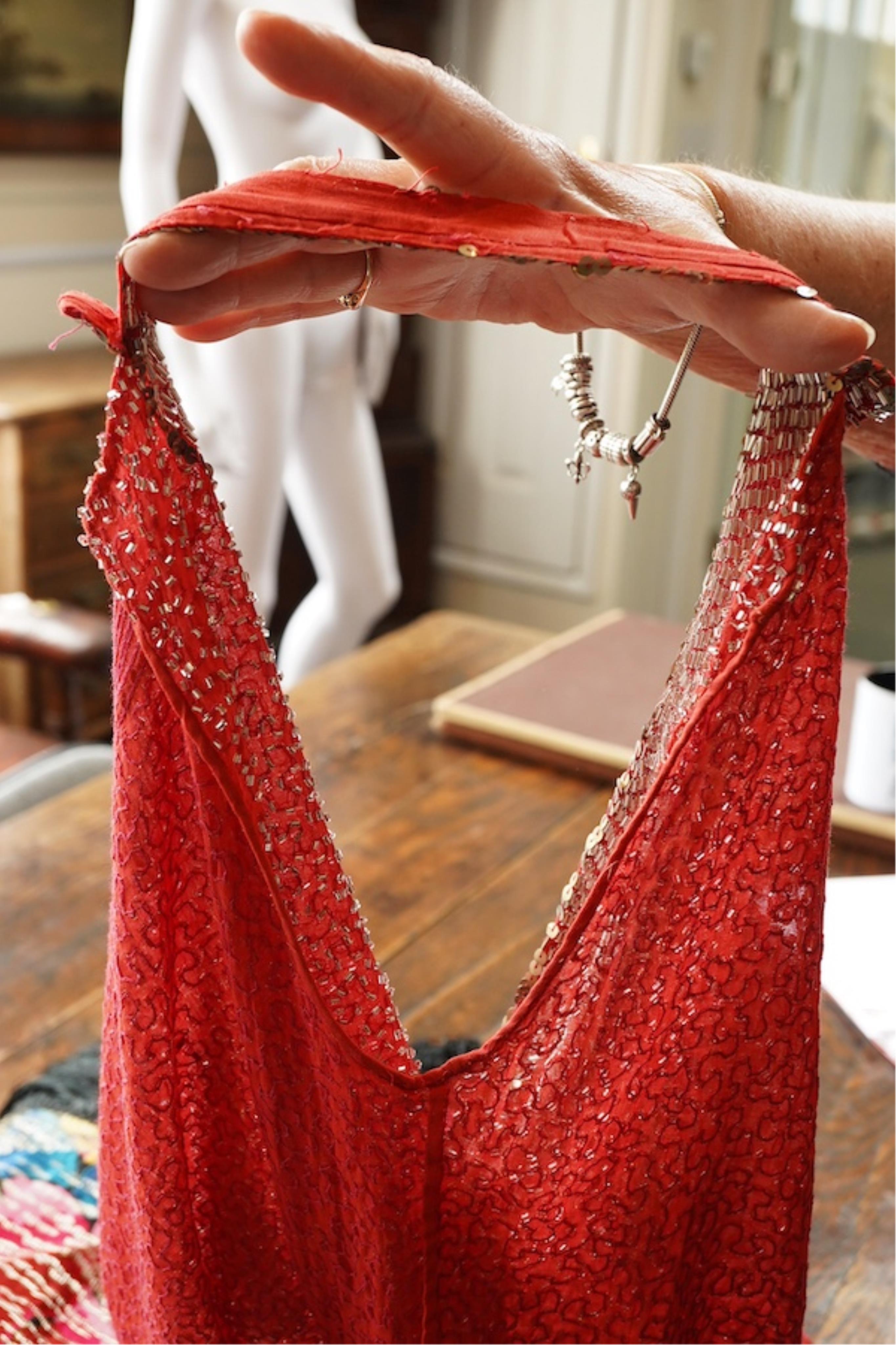 A 1920's red georgette beaded evening dress. Hand beaded and sequinned in white and gold, designed with a dropped waist, handkerchief points and wide beaded border with large stylistic floral motifs. Length 115cm. Condit
